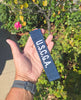 Hand holding a blue U.S.C.G.A. luggage tag with greenery in the background